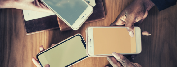 Image of hands holding smartphones on a table.
