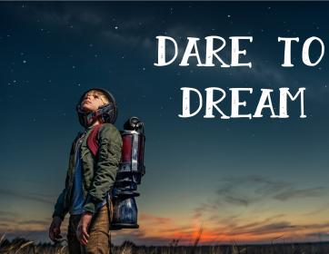 Child dressed up as astronaut looking up towards dark sky. Low setting sun in background.